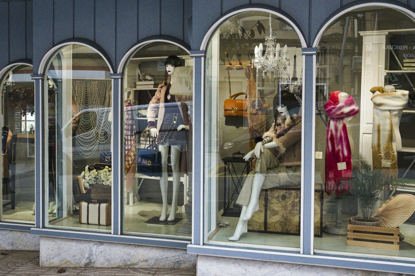 Schaufenster einer Boutique mit Rundbögen, Schaufensterpuppen und Taschen
