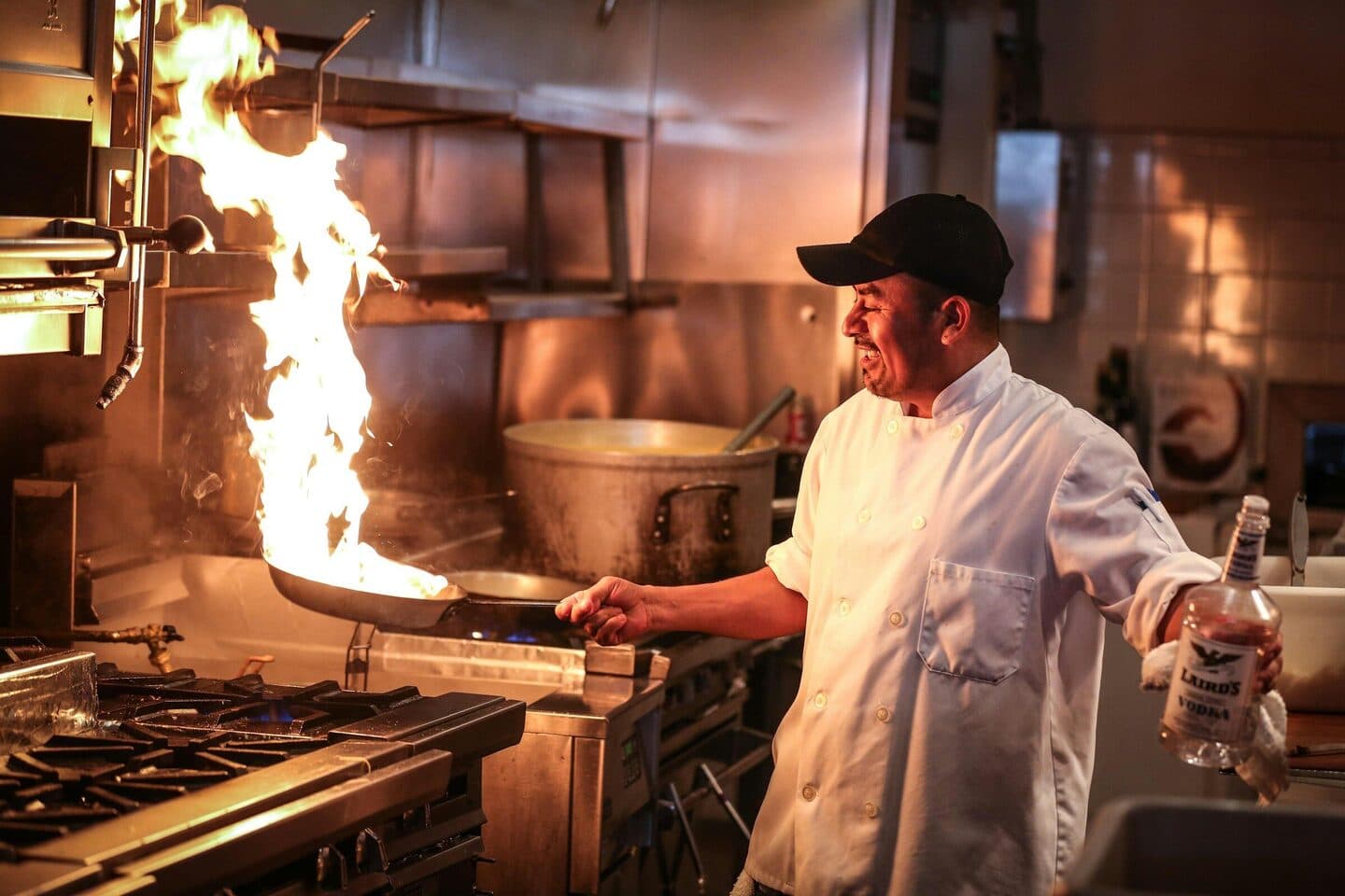 Koch schwenkt am Herd einer Restaurantküche eine Pfanne mit Stichflamme